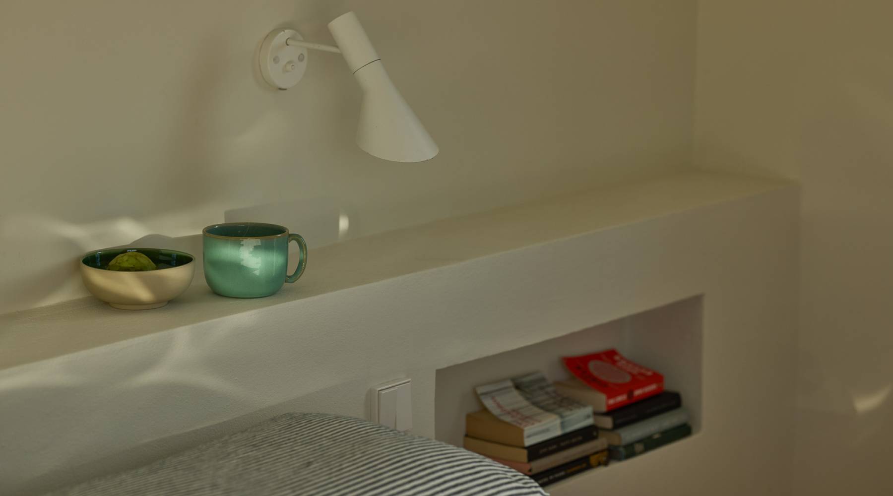 Eine Türkisfarbene Tasse steht neben einer kleinen Schüssel. Die Schüssel ist innen grün und außen Beige. Die Keramik steht auf einem weißen Wand Regal