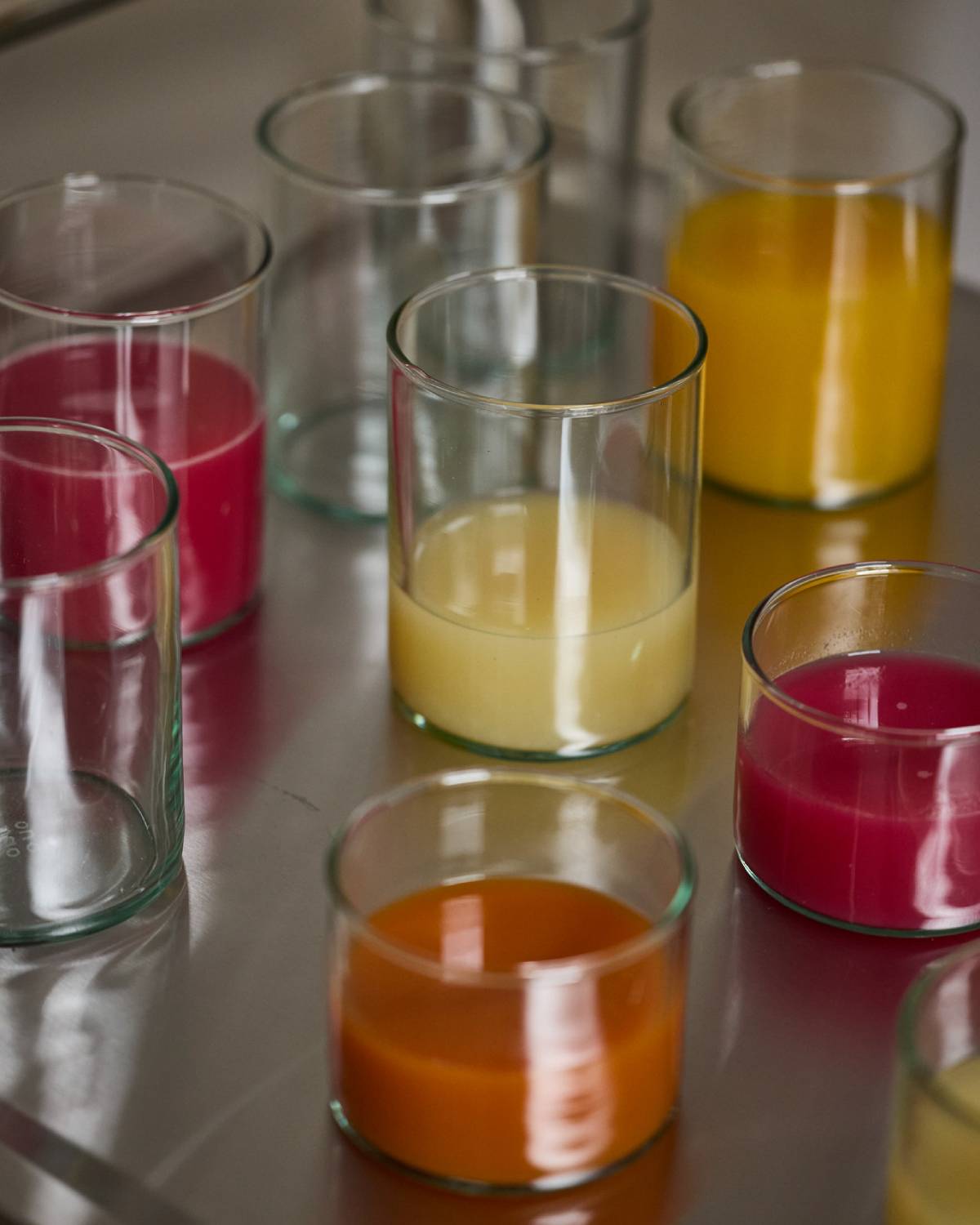 Verschiedene frisch gepresste Säfte in Trinkgläsern auf einer Edelstahlfläche – pink, gelb, orange und cremefarben