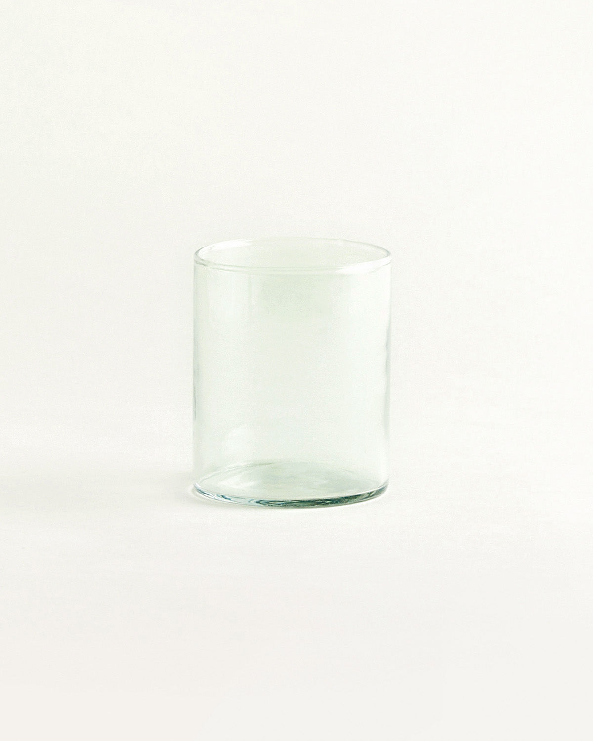 Einzelnes hohes Trinkglas aus grünlichem Glas, gerade Form, vor hellem Hintergrund.