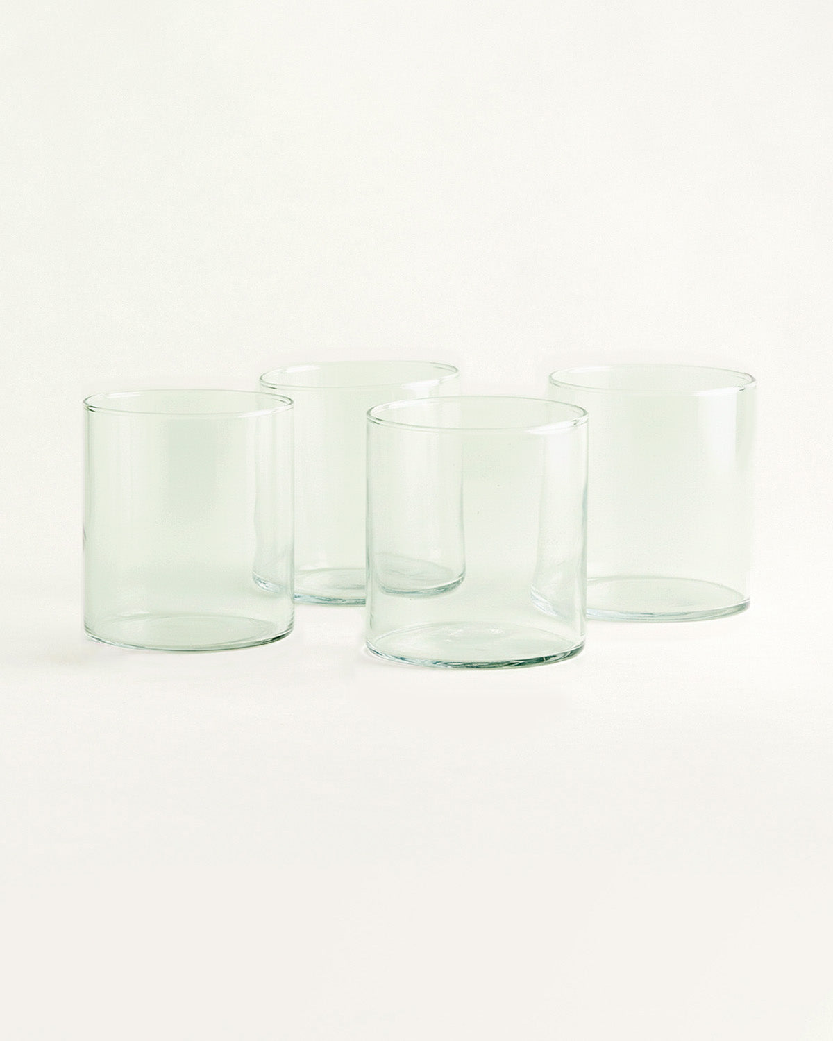 Vier hohe Trinkgläser aus grünlichem Glas vor hellem Hintergrund.