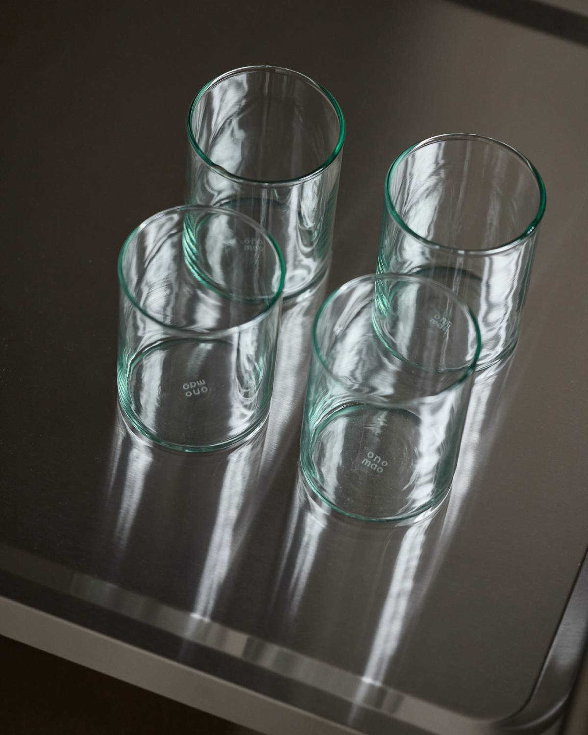 Vier hohe Trinkgläser aus grünlichem Glas mit onomao-Prägung, von oben auf einer dunklen Fläche.